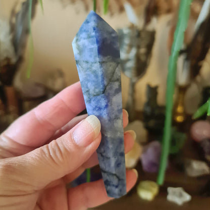 A sodalite crystal held in a person's hand, with a bluish-green color and a rough, natural appearance.