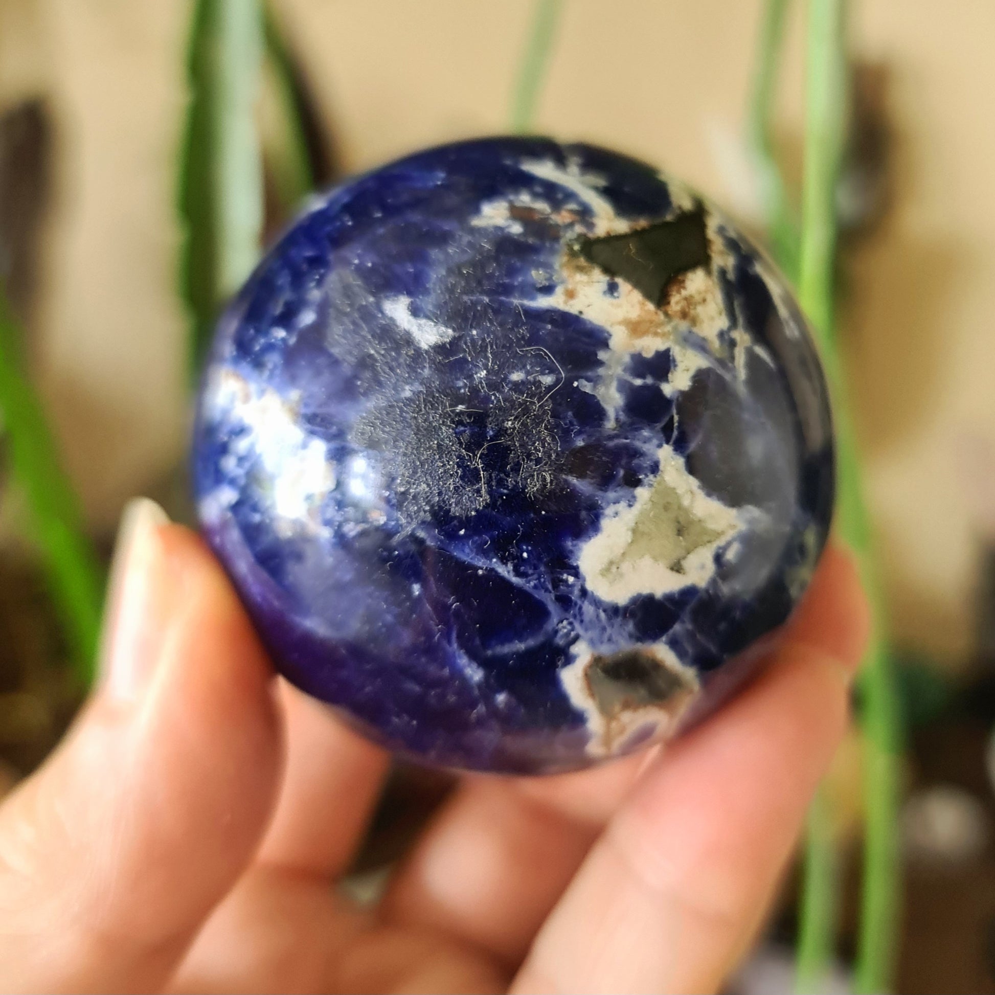 A sodalite crystal sphere held in a person's hand, with a deep blue color and natural mineral patterns.