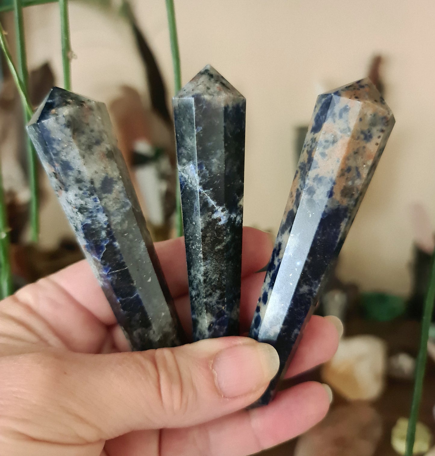 Three sodalite wands with a glossy blue and brown coating, held in a person's hand.