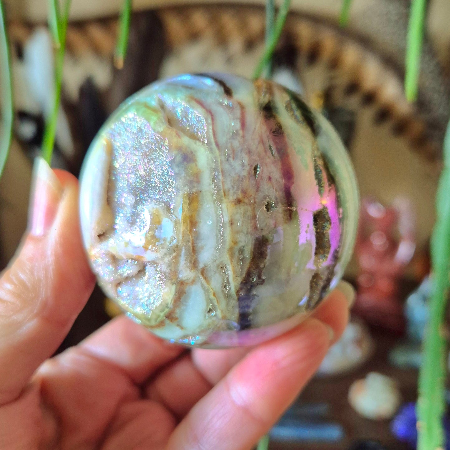 A hand holding a Sphalerite Aura Sphere with a marbled multicolor pattern.
