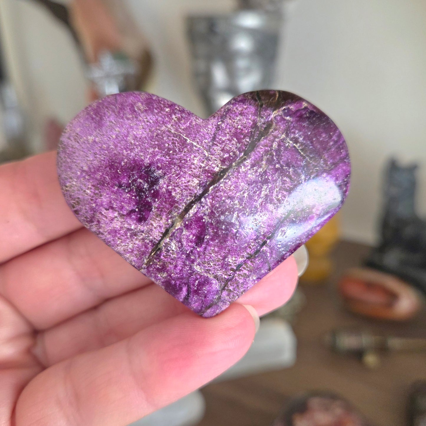 Heart-shaped purple crystal held in a hand with a blurred background