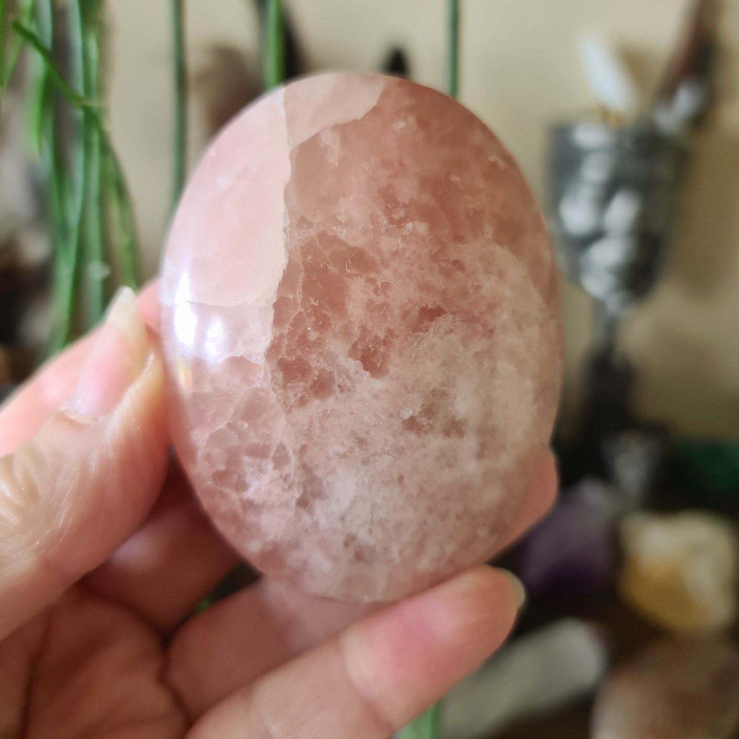 A person holding a polished pink calcite stone, kidney-shaped, with a smooth and shiny surface.
