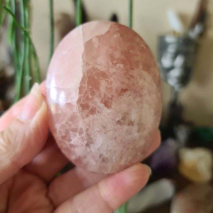 A person holding a polished pink calcite stone, kidney-shaped, with a smooth and shiny surface.