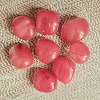 A collection of Strawberry Obsidian stones with a red/pink color, arranged on a wooden surface.