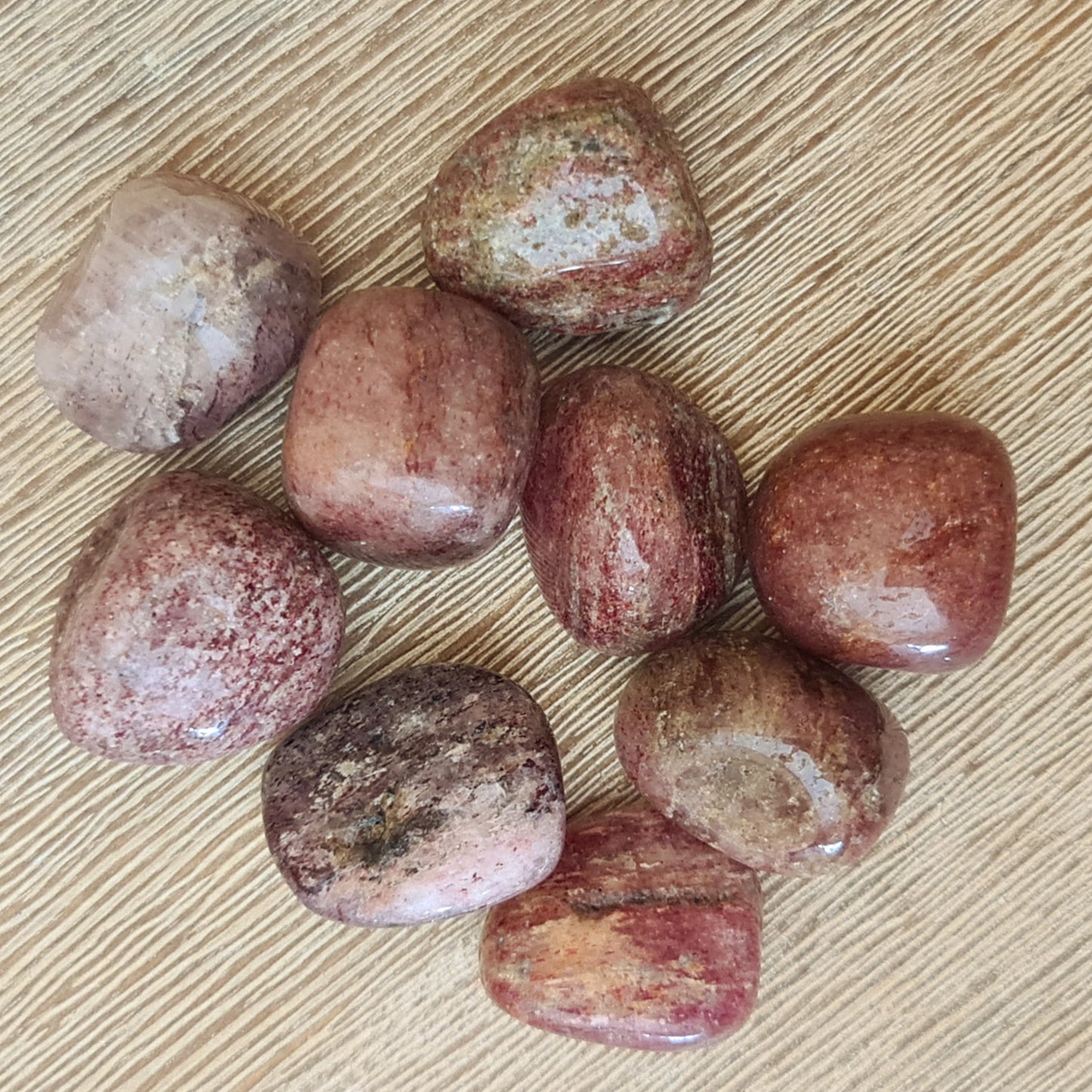 A collection of polished Strawberry Quartz tumbles with varying shades of pink and natural color patterns.