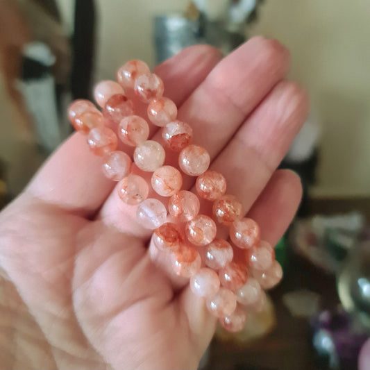 A hand holding a strawberry quartz bracelet with pink and clear beads.