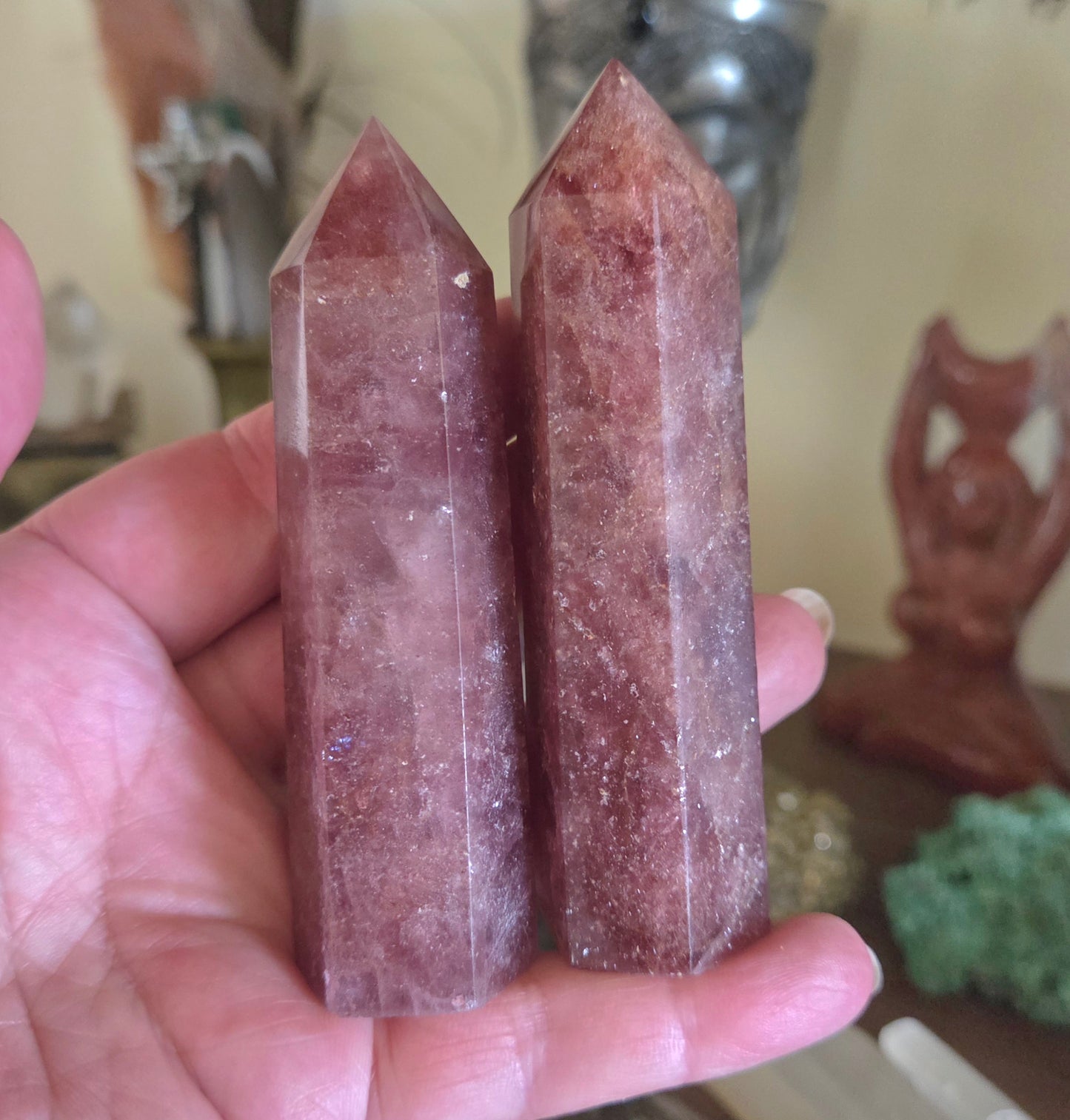 Two pink crystal sticks held in a hand with a blurred background