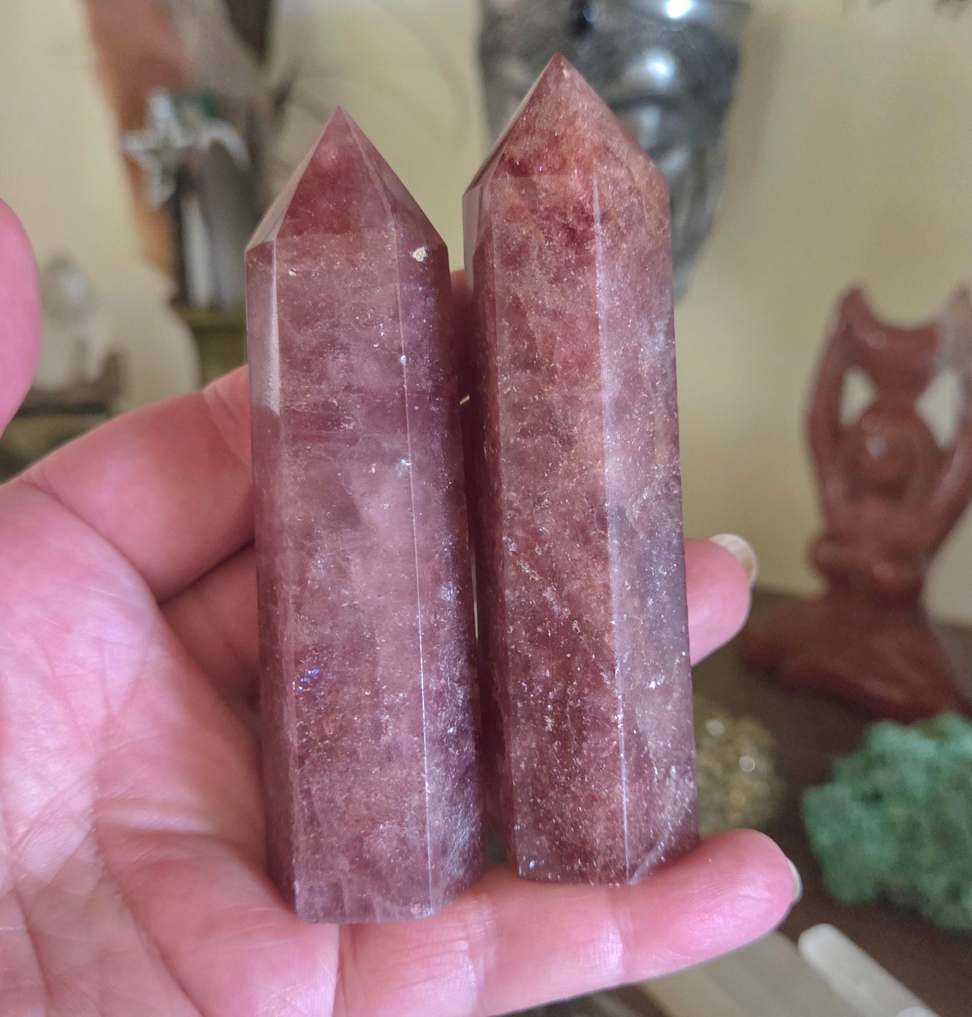 Two pink crystal sticks held in a hand with a blurred background