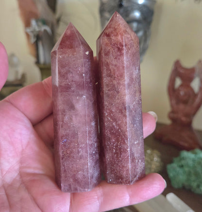 Two pink crystal sticks held in a hand with a blurred background