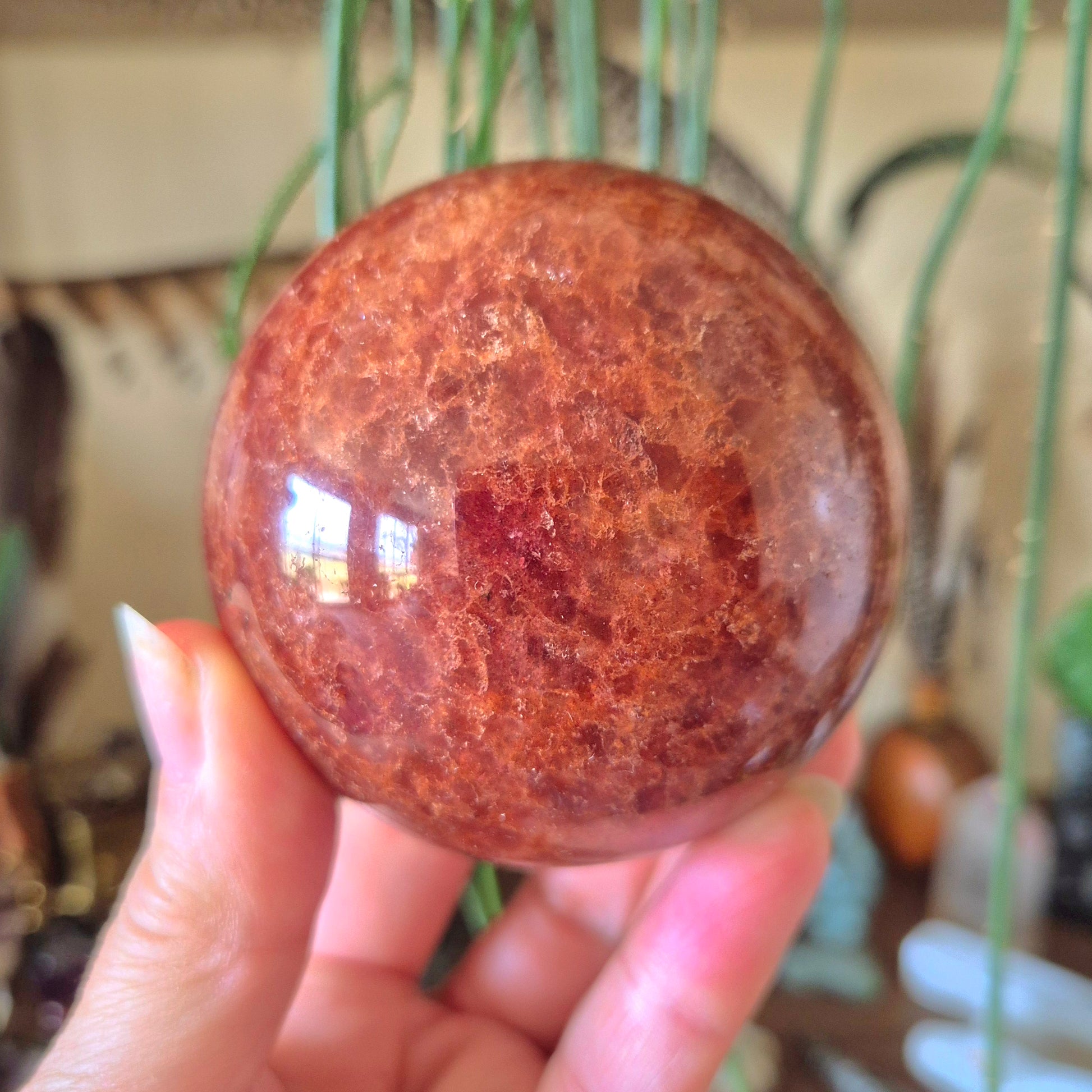 A polished Strawberry Quartz sphere held in a person's hand, with a reflective and textured surface.