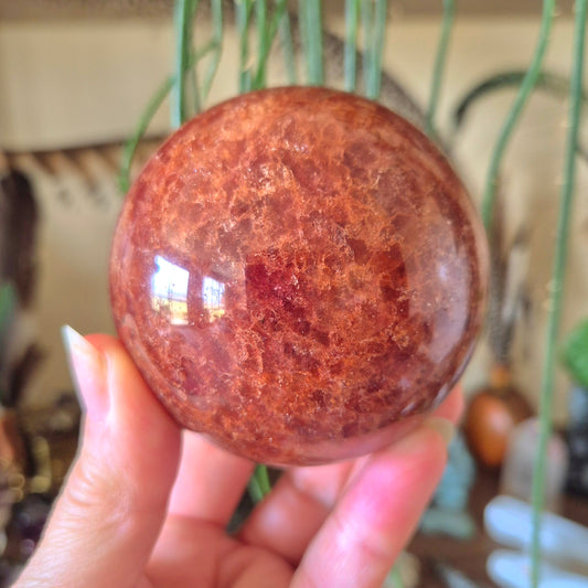 A polished Strawberry Quartz sphere held in a person's hand, with a reflective and textured surface.