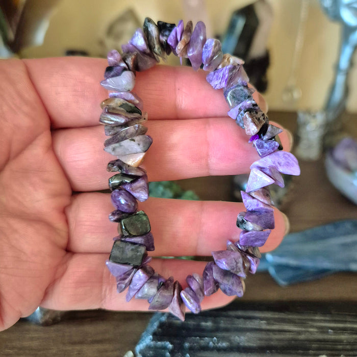 A hand holding a multicolored sugalite bracelet with various shapes and sizes of gemstones.