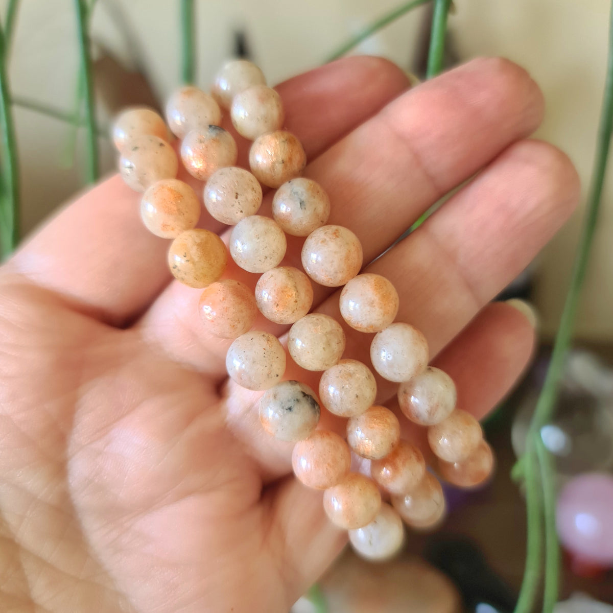 A hand holding a sunstone bead bracelet with a mix of orange, brown, and translucent colors.