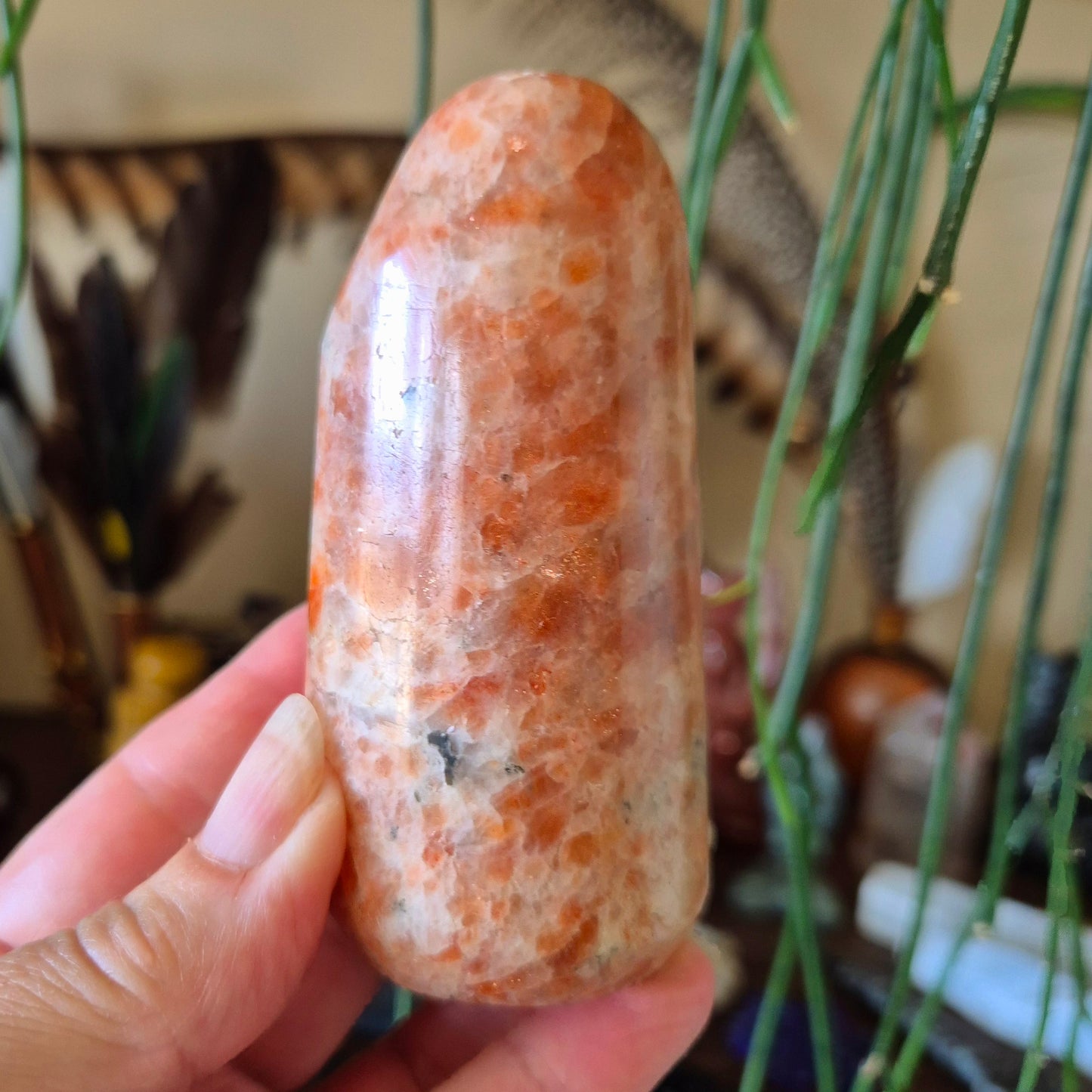 A hand holding a polished sunstone freeform with a glossy surface.