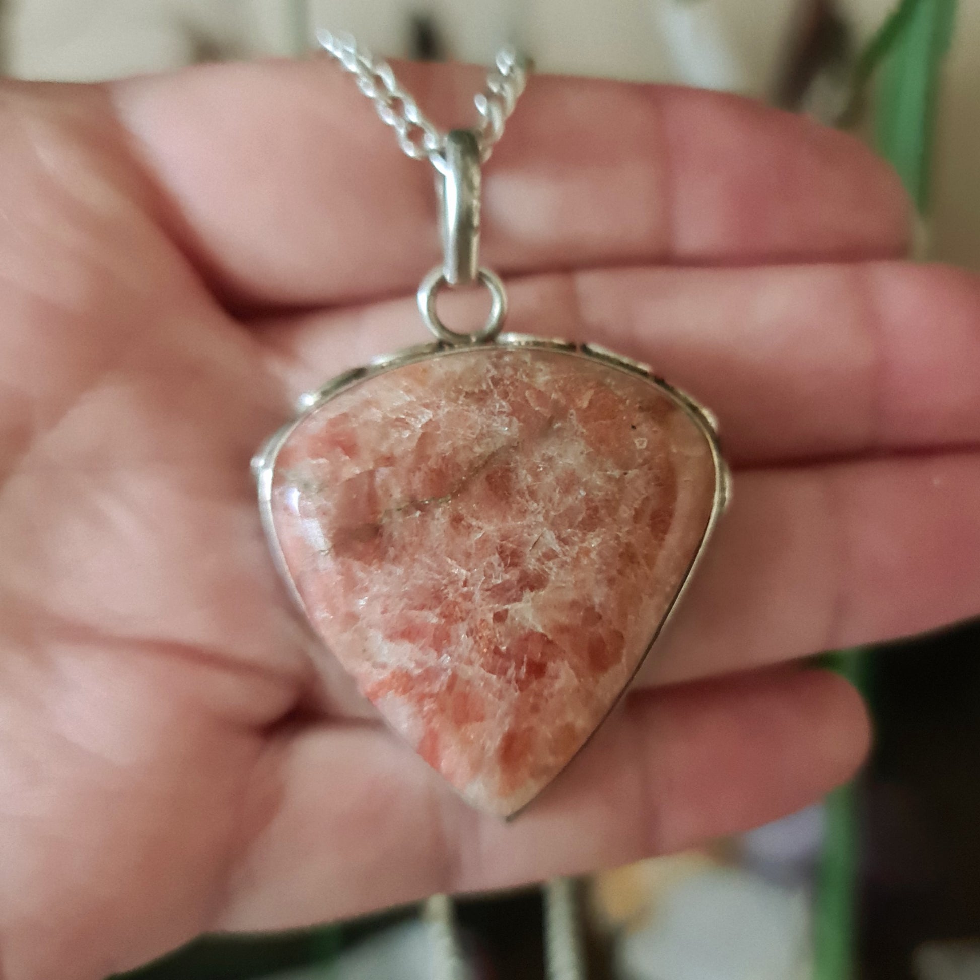 A sterling silver pendant with a round sunstone gemstone in the center, held in a person's hand.