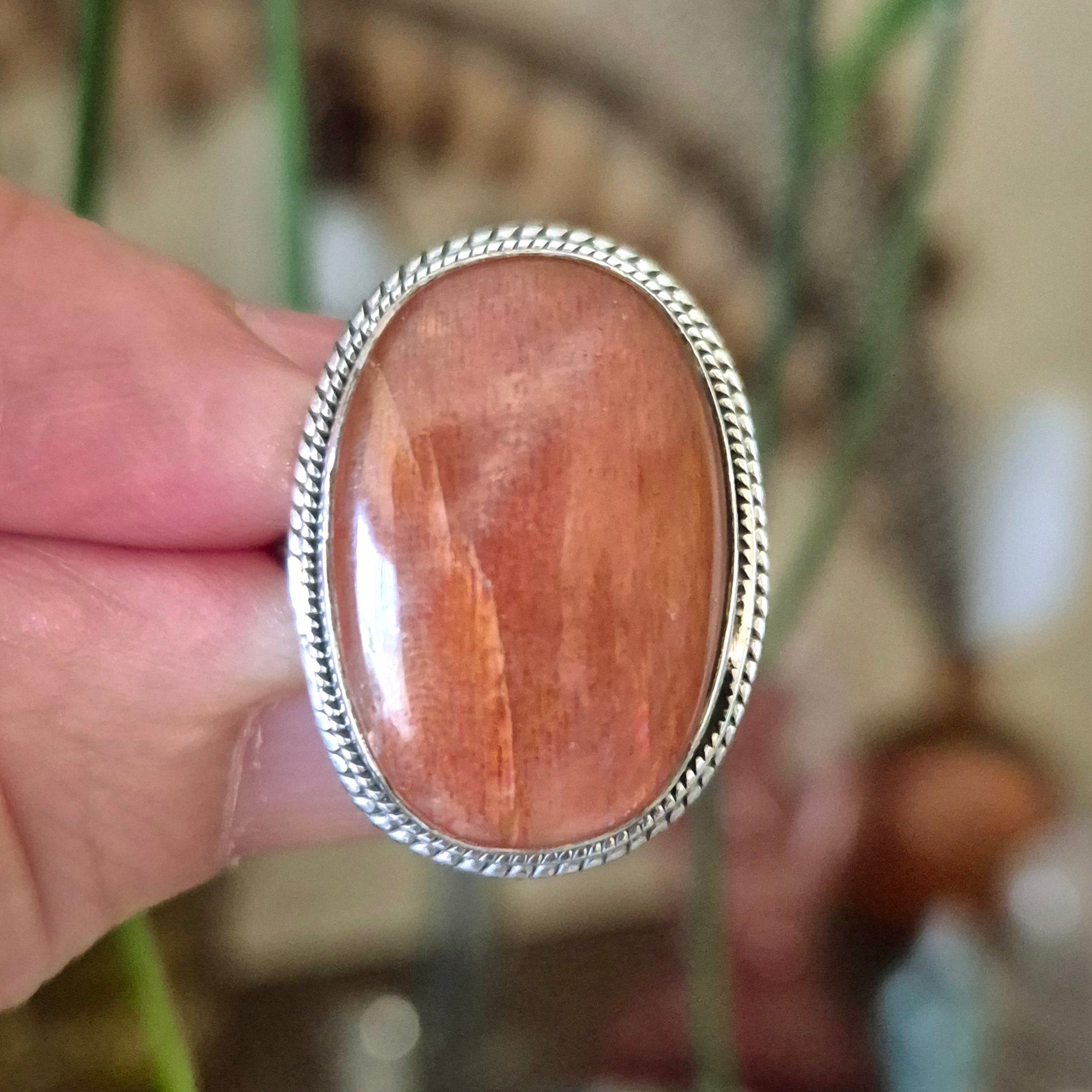 A hand holding a round sunstone ring with a metallic band.