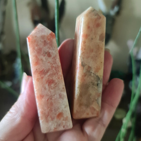 A polished sunstone with a reddish-orange coloring, held in a person's hand.