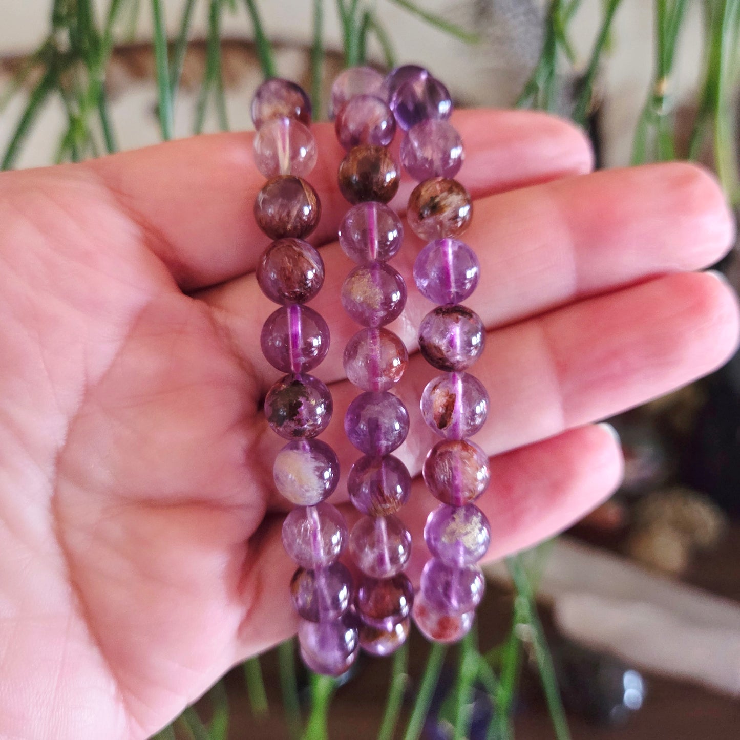 Hand holding a stack of purple beaded bracelets with a blurred natural background
