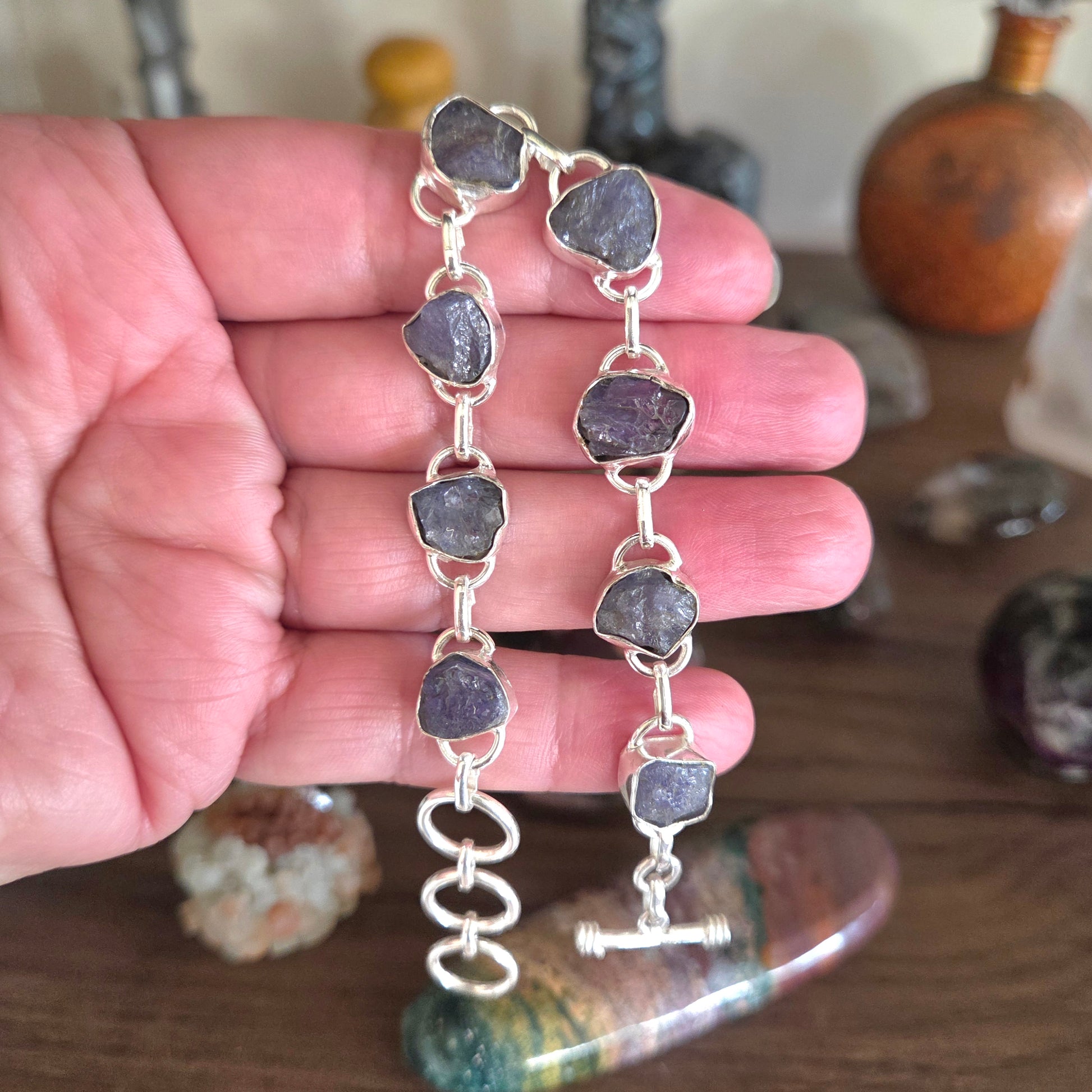 Hand holding a silver bracelet with purple stones on a wooden surface