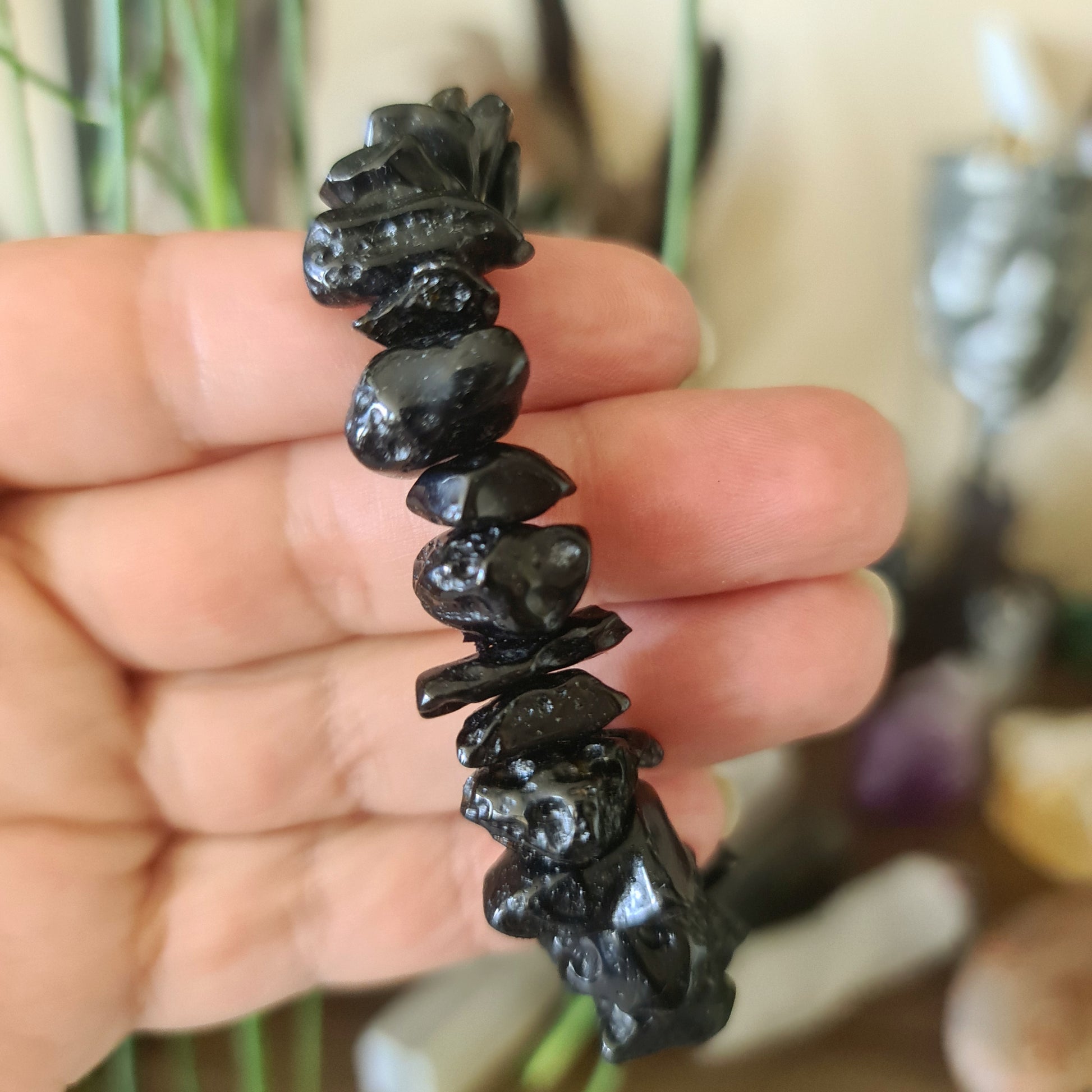 A hand holding a bracelet made of black tektite stones with a blurred background.