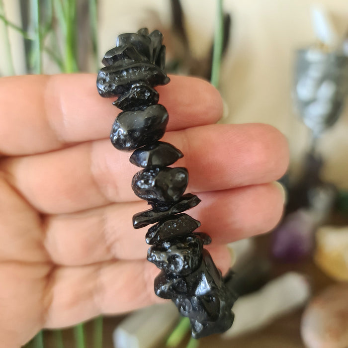 A hand holding a bracelet made of black tektite stones with a blurred background.