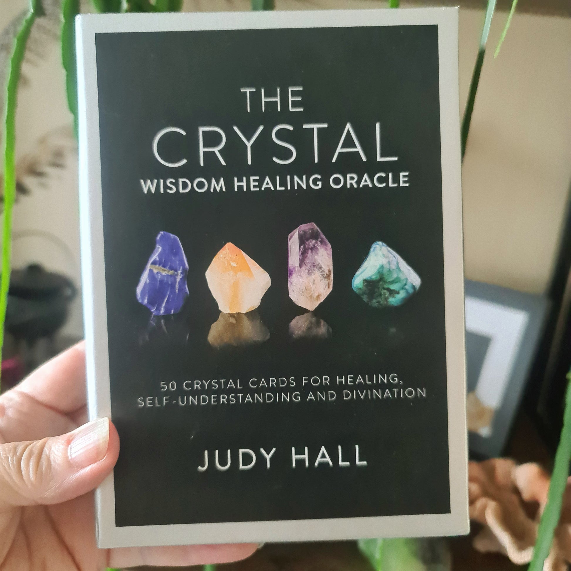 A book titled 'The Crystal Wisdom Healing Oracle' by Judy Hall, featuring a black cover with illustrations of various colorful crystals.