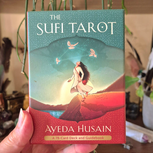 A hand holding a book titled 'The Sufi Tarot' by Aeyda Husan, featuring an illustration of a woman in a mystical pose against a sufi-themed backdrop with birds and a crescent moon.