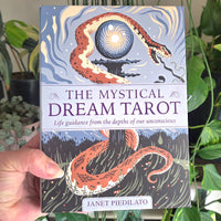 A hand holds a boxed tarot card deck titled "The Mystical Dream Tarot" by Janet Piedilato. The box art shows a stylized snake wrapping around a glowing orb against a blue sky and dark forest background.