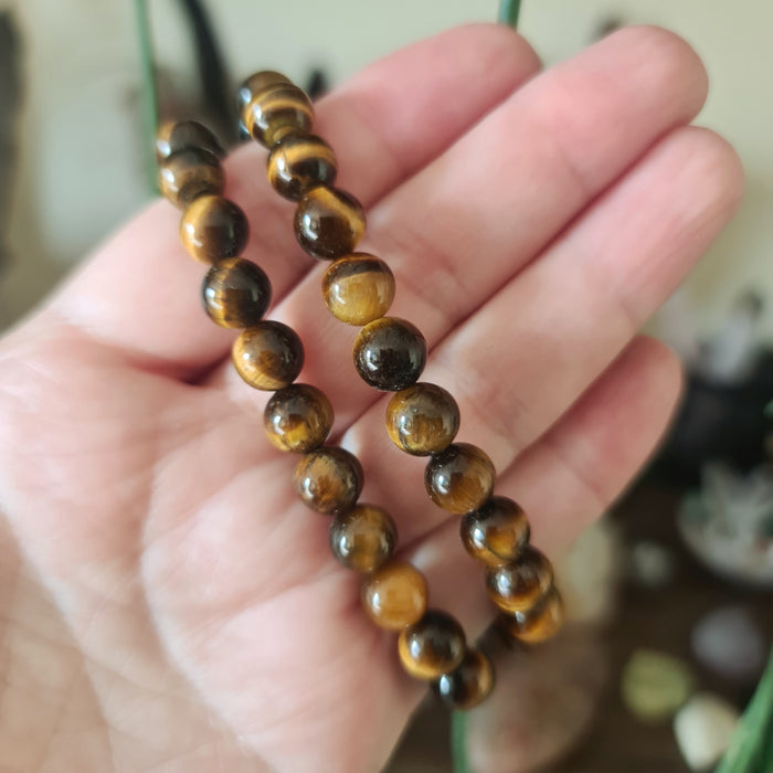 A person holding a tiger eye beaded bracelet with a brownish-yellow color.