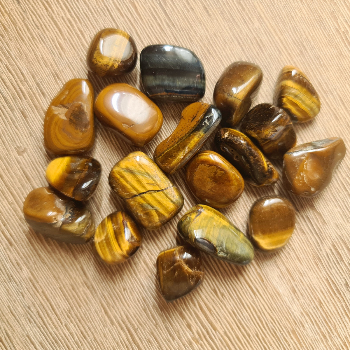 A collection of polished Tiger Eye stones with a smooth, rounded appearance, displayed on a wooden surface.