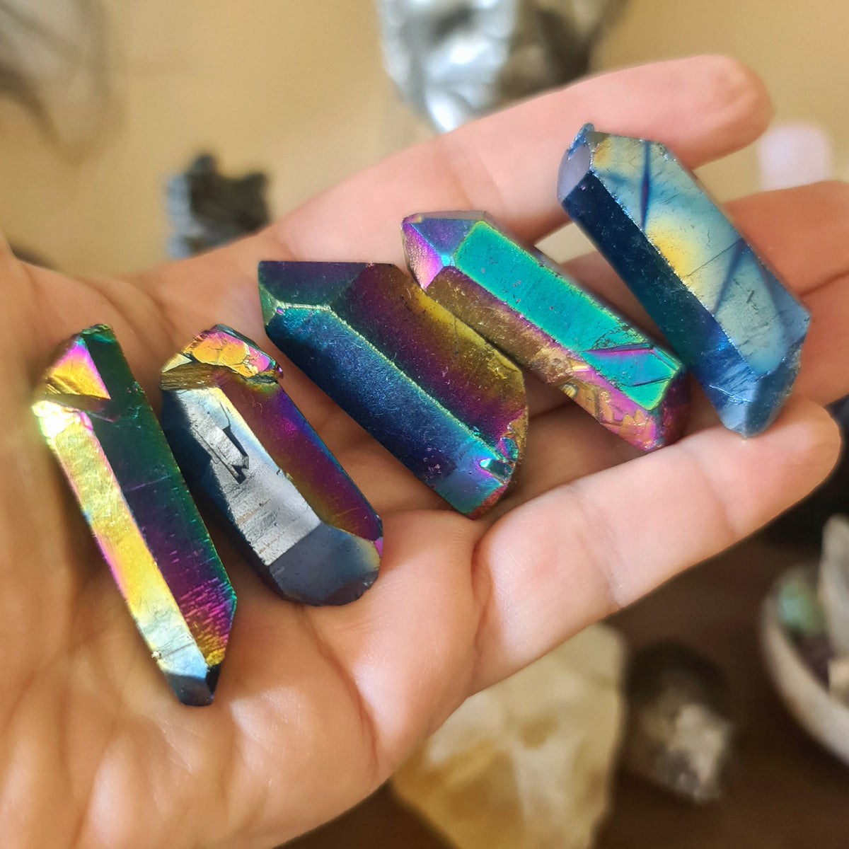 A hand holding a multicolored titanium aura point used for crystal grids and healing.