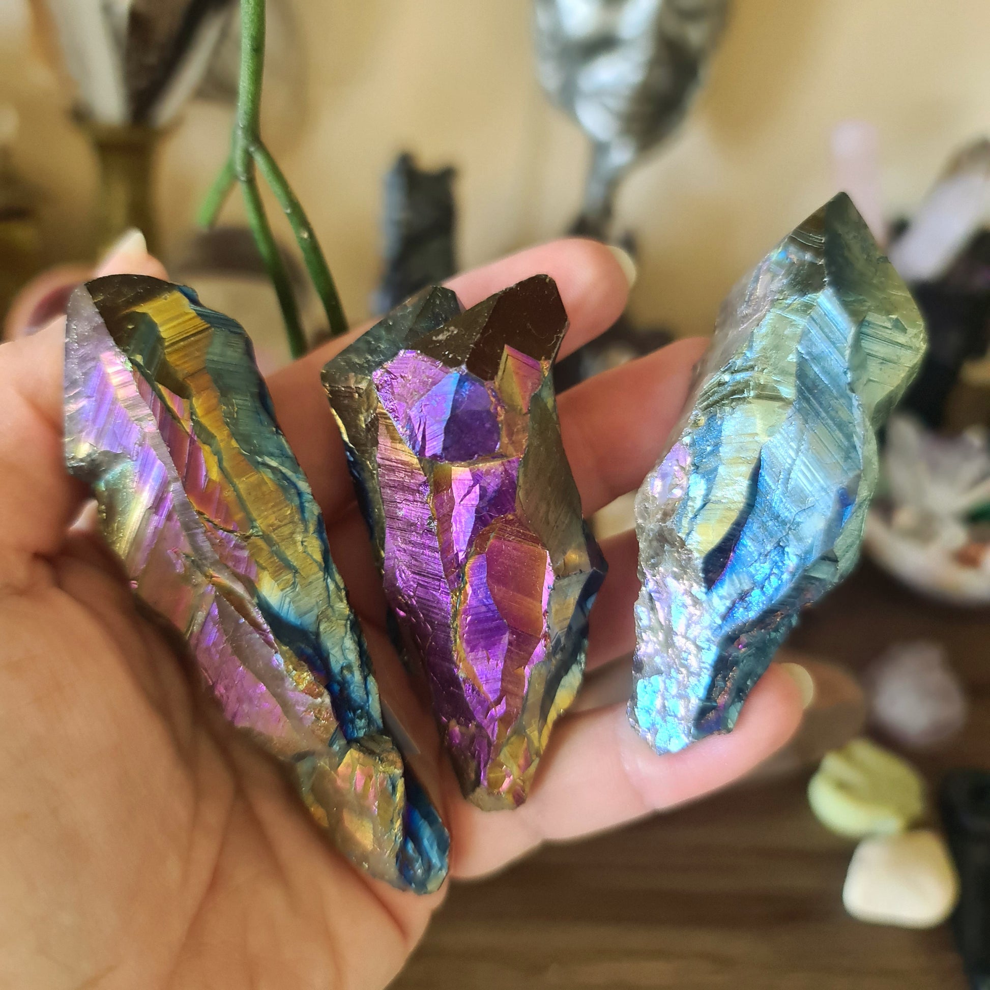 A hand holding a multicolored titanium aura quartz crystal, with a rainbow-like sheen.