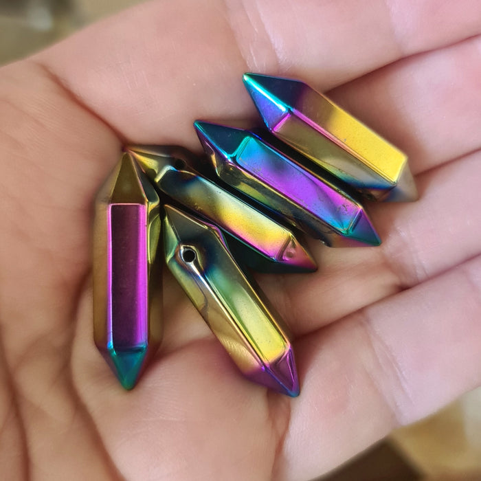 A hand holding a titanium pendant with a multicolored aura stone attached to a gold-colored titanium metal cap.