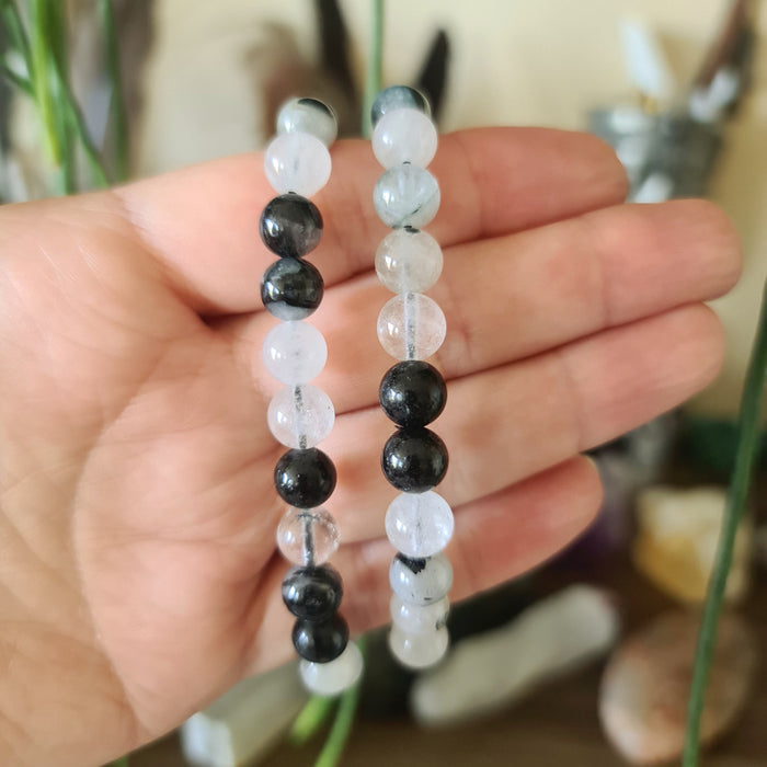 A hand holding a tourmaline quartz bracelet with black and clear beads.