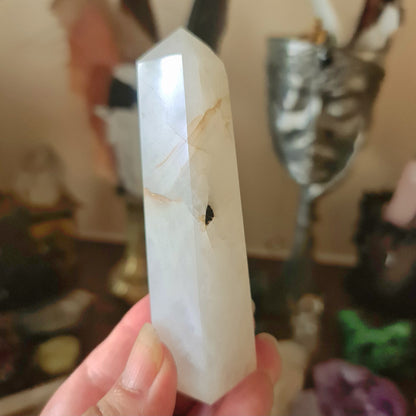 A medium-sized white Tourmaline Quartz crystal held in a person's hand, with a reflective surface and a pointy top.