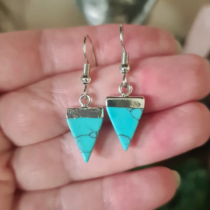 A hand holding a triangular blue crystal earring with a silver cap and hook.