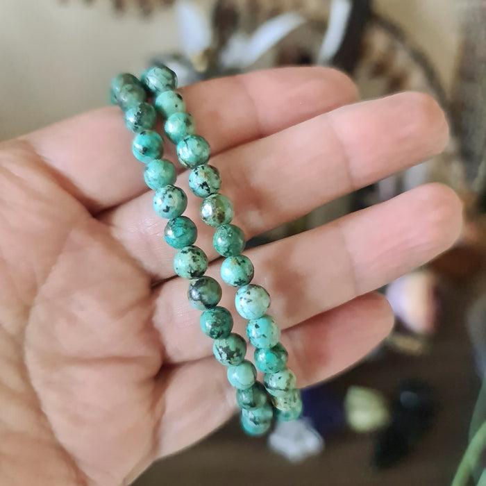 A hand holding a turquoise beaded bracelet with a pattern of dots and veins.