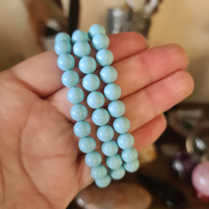 A turquoise beaded bracelet held in a person's hand, with a variety of beads displayed in a semi-circular arrangement.