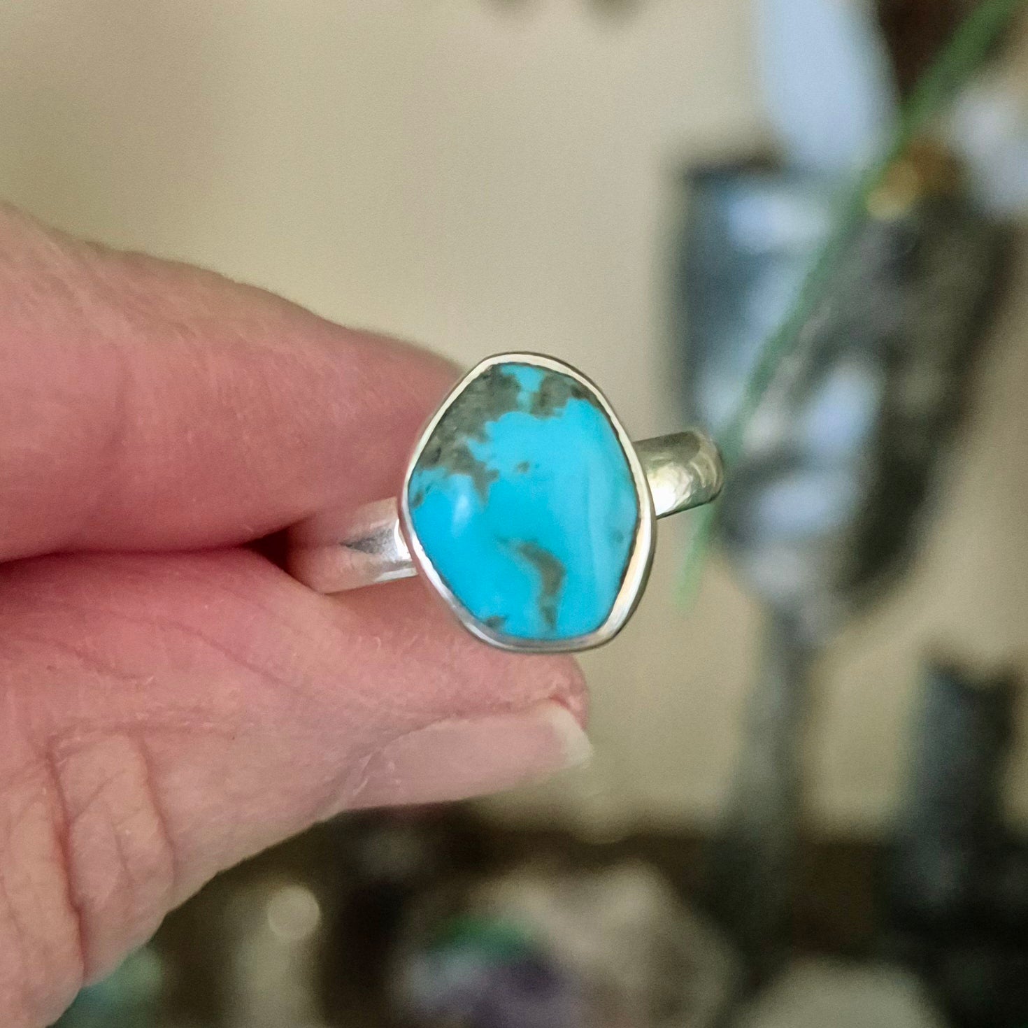 A person holding a turquoise ring with a metallic band, with the turquoise stone displaying web-like patterns.