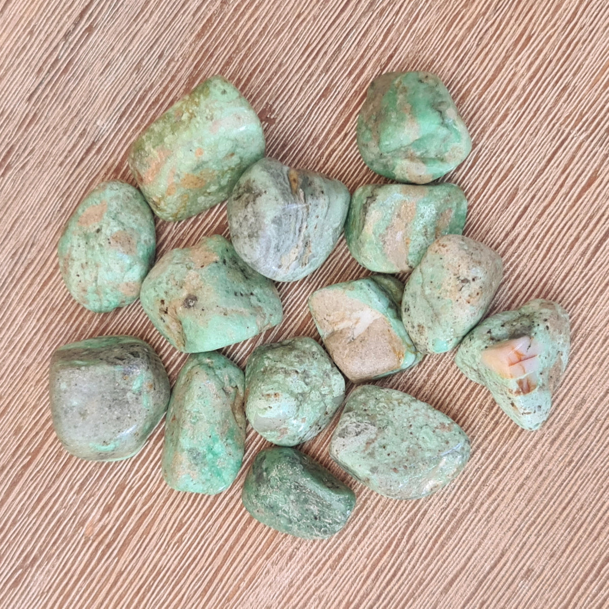 A collection of Variscite tumble stones displayed on a wooden surface.