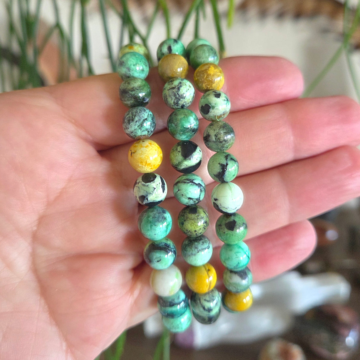 Hand holding a stack of green and yellow beaded bracelets with a blurred background