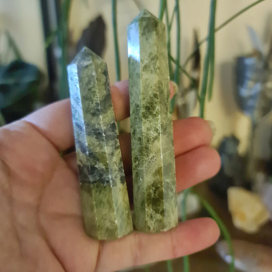 A hand holding a Vessonite Point crystal, with a blurred background suggesting indoor setting