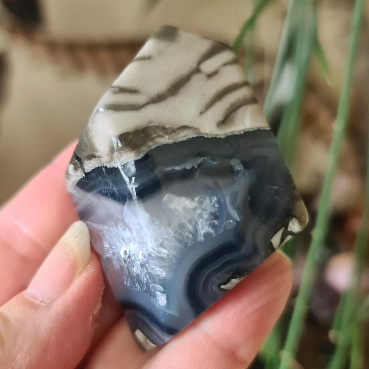 A freeform-shaped Volcano Agate stone held in a person's hand, displaying patterns of black, gray, and white.