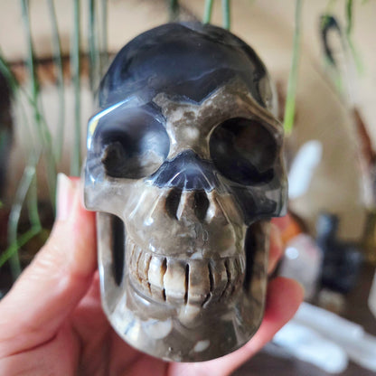 A hand holding a polished agate skull, displaying a mix of gray and black colors.