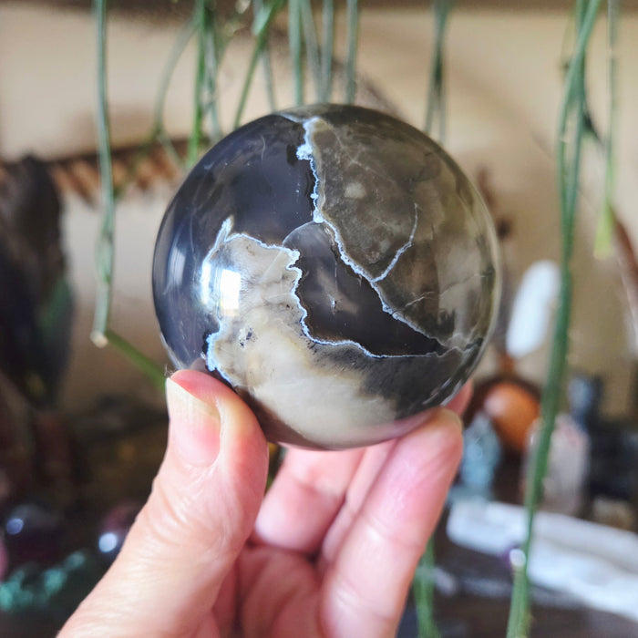 A hand holding a polished sphere of Volcano Agate with a visible pattern resembling volcanic activity.