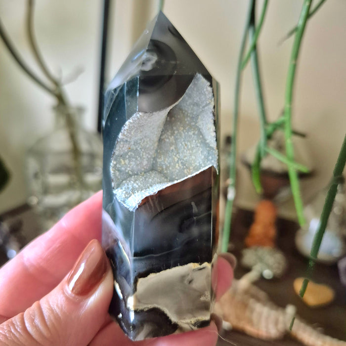 A close-up of a Volcano Agate crystal with a black and gray color scheme, held in a person's hand.