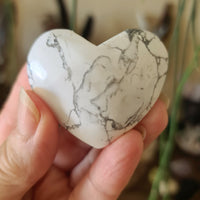 A heart-shaped white howlite stone held in a person's hand, with a marbled white and gray appearance.