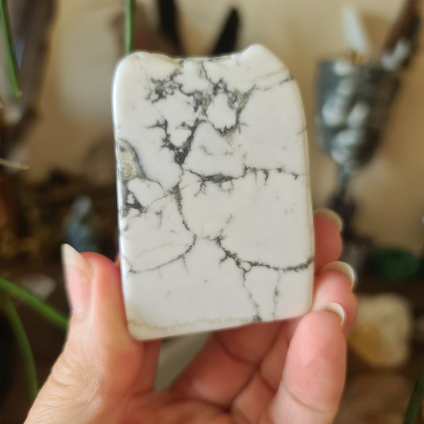 A hand holding a white howlite tile with a marbled pattern.