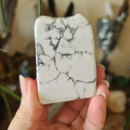 A hand holding a white howlite tile with a marbled pattern.