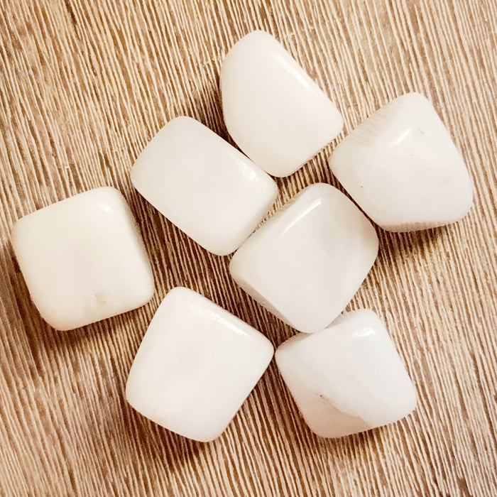 A collection of eight polished white jade tumble stones arranged on a wooden surface.
